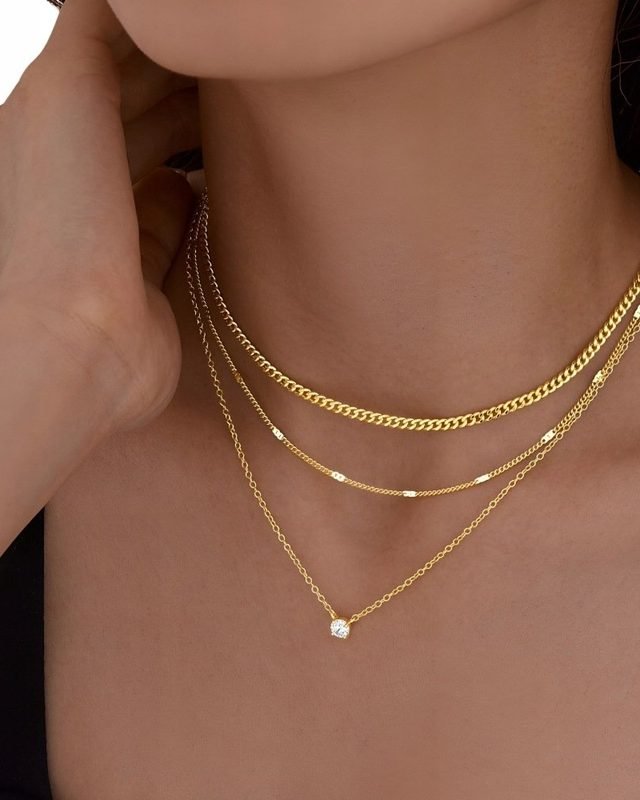 Three layered gold-tone chains: curb, bar station and a fine chain with a solitaire